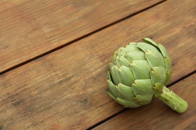 Photo of Fresh raw artichoke on wooden table. Space for text