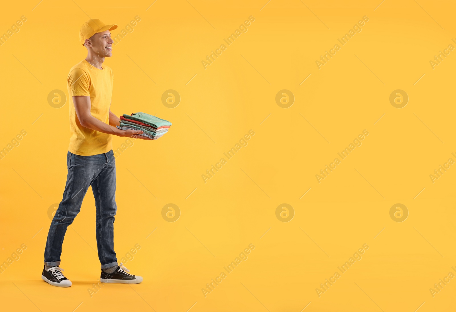 Photo of Dry-cleaning delivery. Happy courier holding folded clothes on orange background, space for text