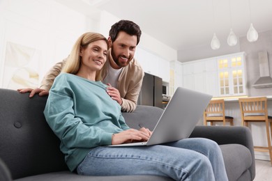 Happy couple using laptop on sofa at home, low angle view