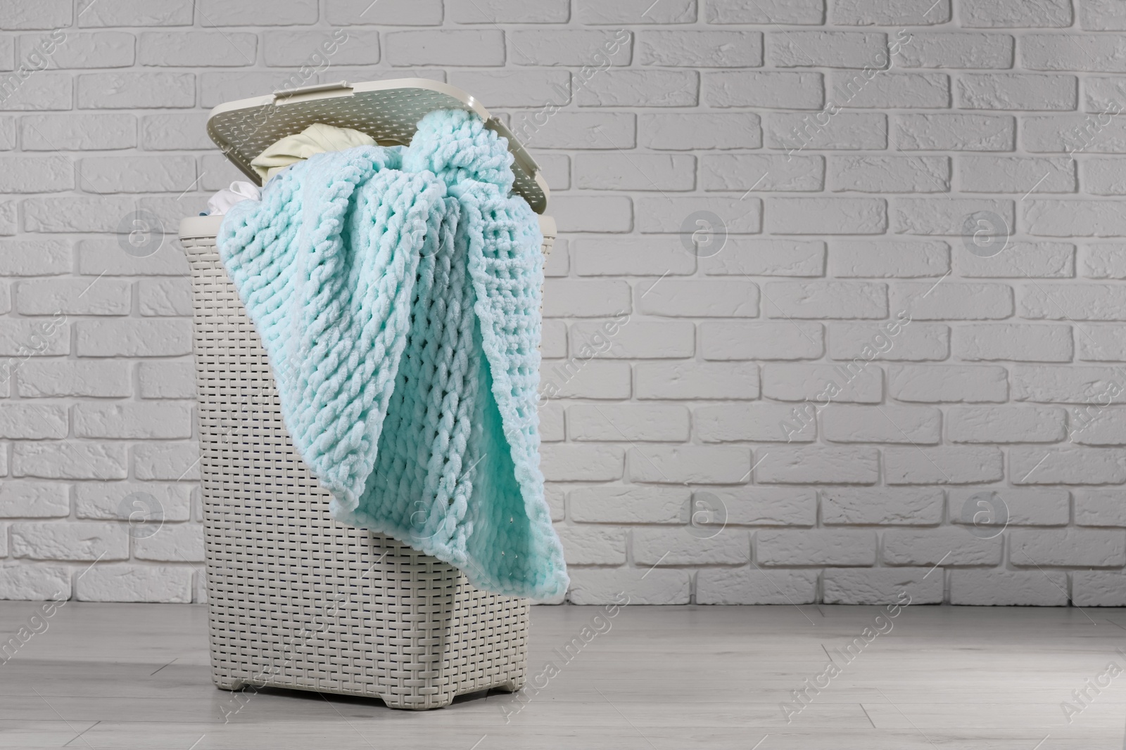 Photo of Laundry basket with clothes near white brick wall. Space for text