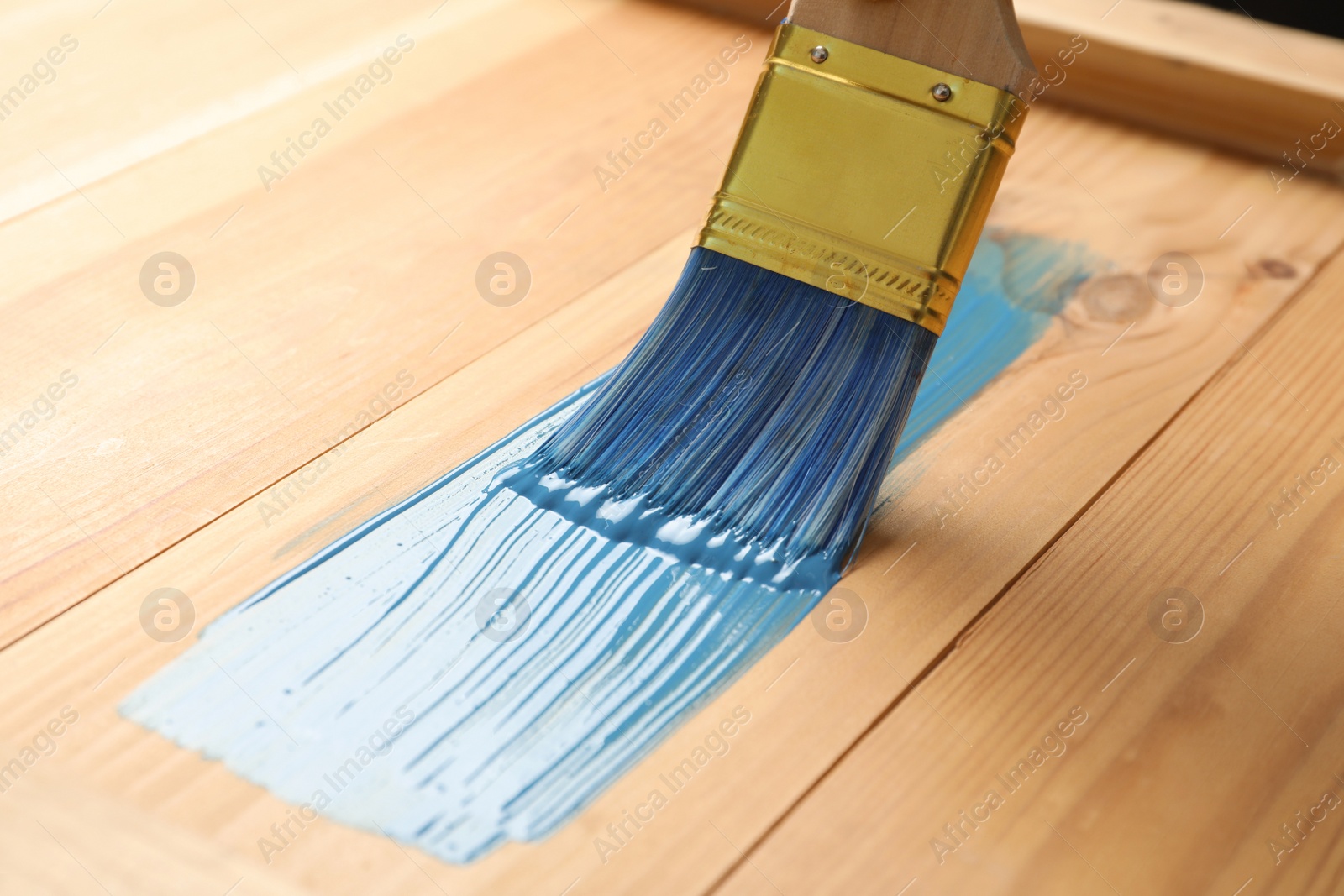 Photo of Applying blue paint onto wooden surface, closeup