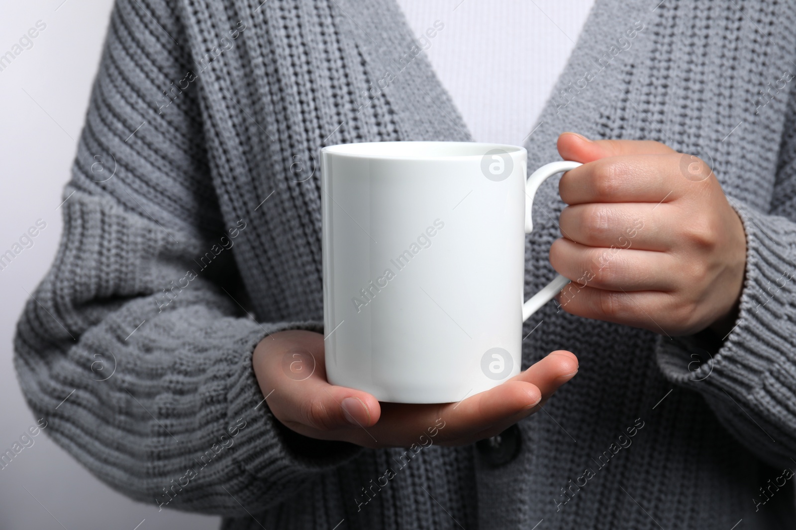 Photo of Woman holding white mug on light gray background, closeup. Mockup for design