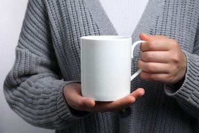 Woman holding white mug on light gray background, closeup. Mockup for design