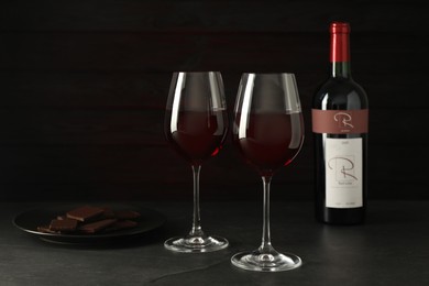 Glasses and bottle of red wine with chocolate on grey table