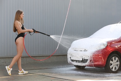 Young woman in swimsuit with high pressure water jet cleaning automobile at car wash