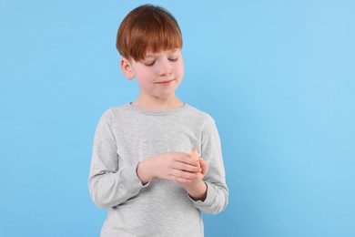 Little boy putting sticking plaster onto finger against light blue background