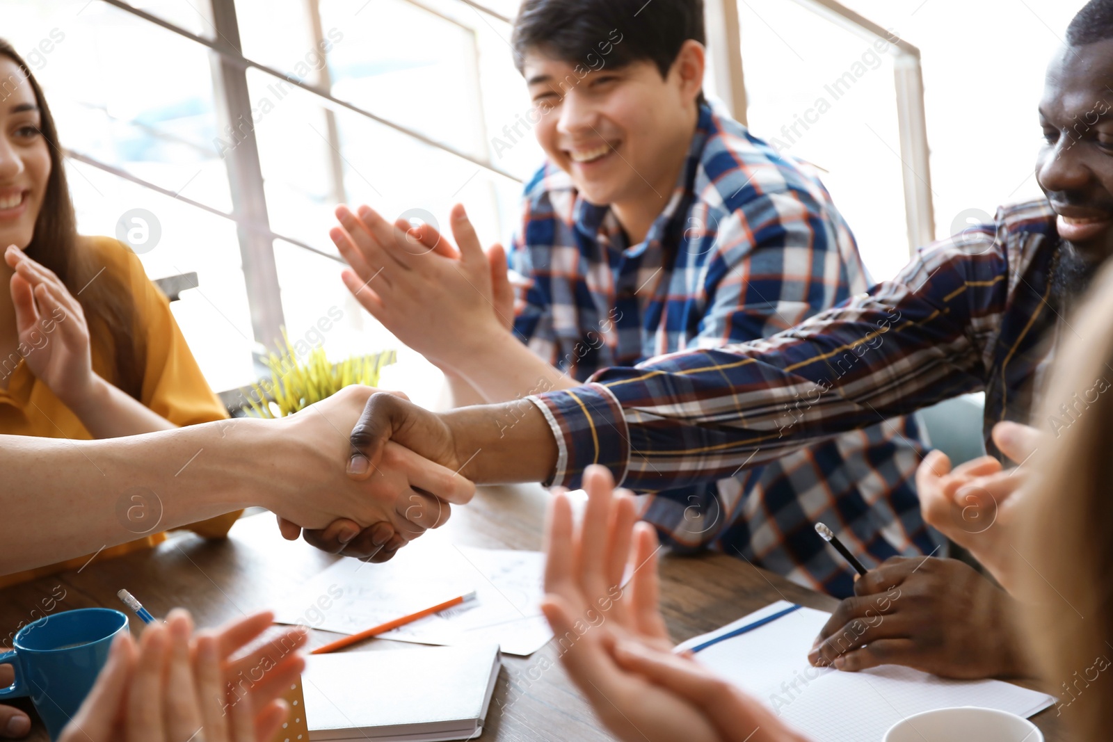 Photo of Young men shaking hands at table. Unity concept