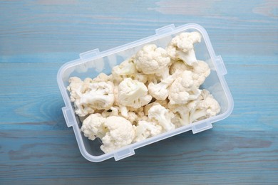 Plastic container with different fresh cut cauliflower on light blue wooden table, top view