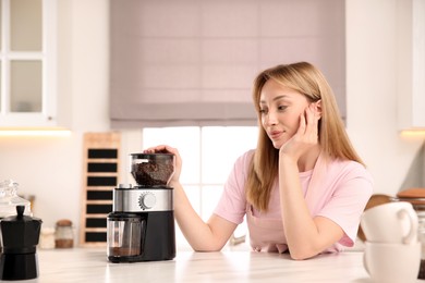 Photo of Young woman using electric coffee grinder in kitchen