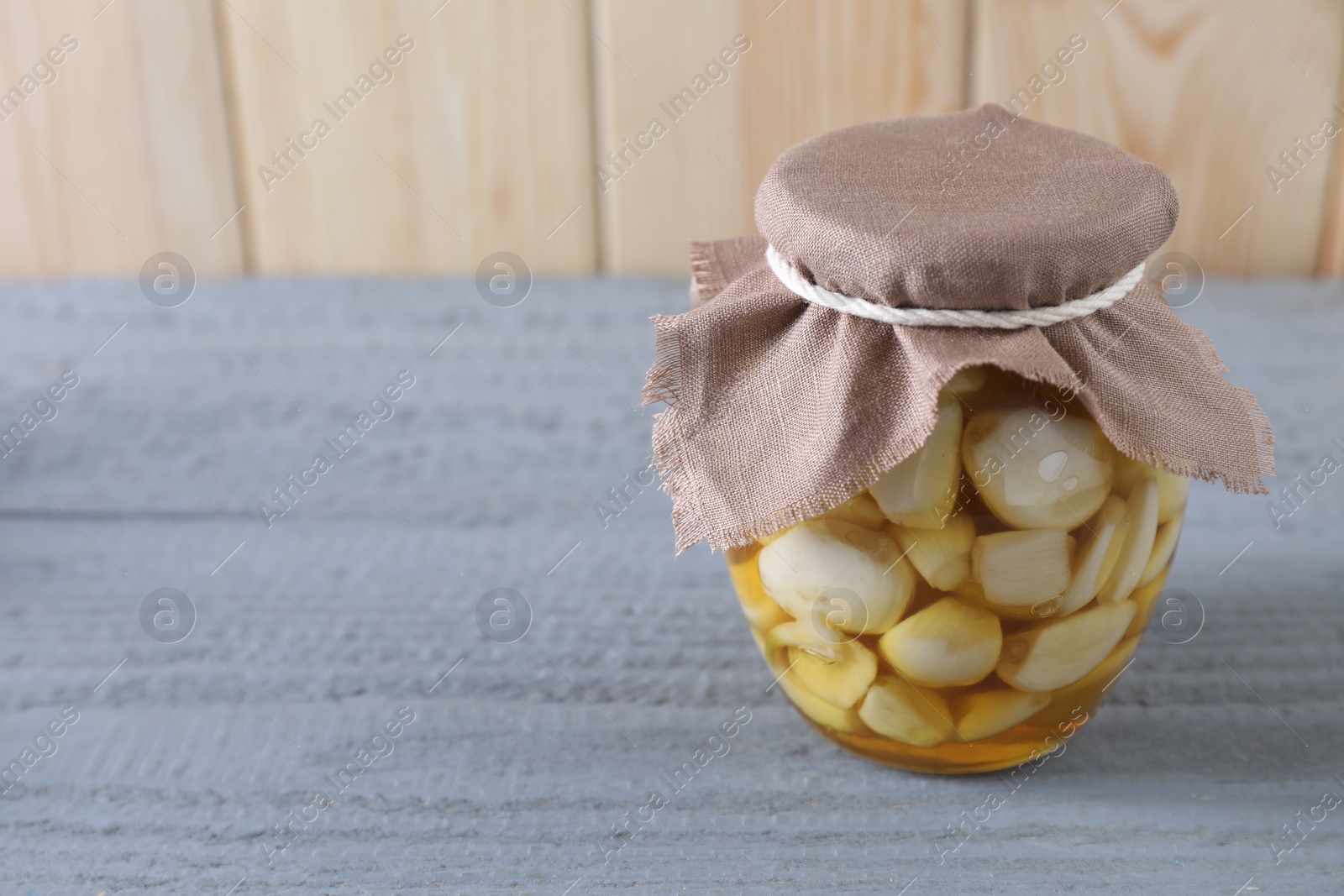 Photo of Garlic with honey in glass jar on grey wooden table. Space for text