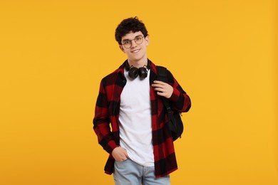 Photo of Portrait of student with backpack, headphones and glasses on orange background