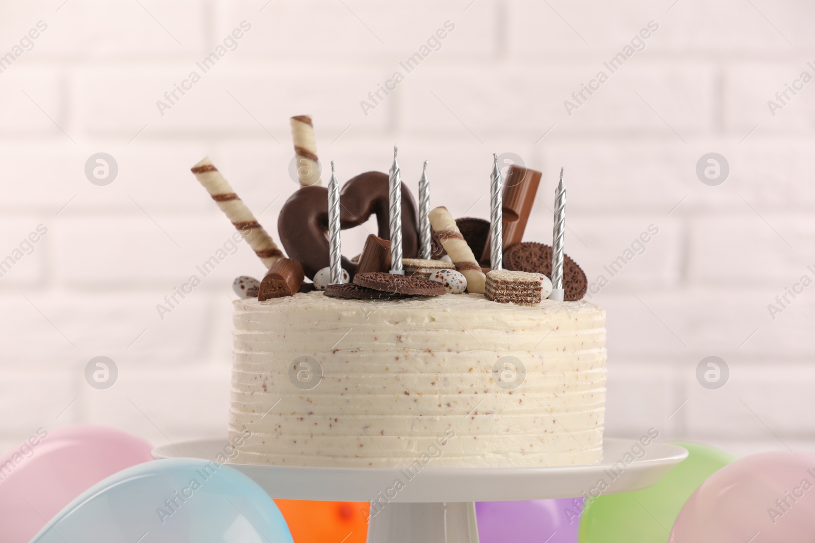 Photo of Delicious cake decorated with sweets and candles against white brick wall