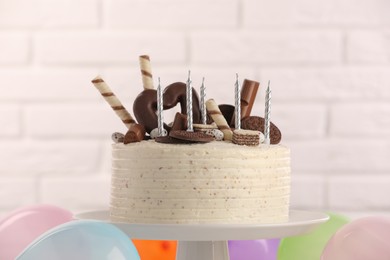 Photo of Delicious cake decorated with sweets and candles against white brick wall