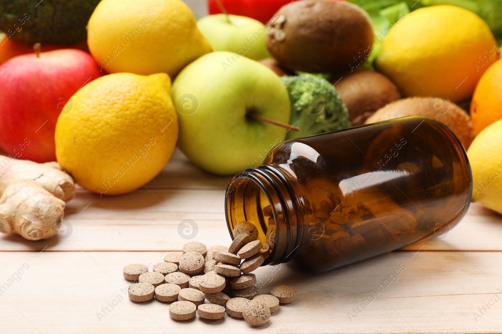 Photo of Dietary supplements. Overturned bottle with pills near food products on light wooden table