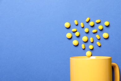 Photo of Yellow candies and cup on blue background, flat lay. Space for text