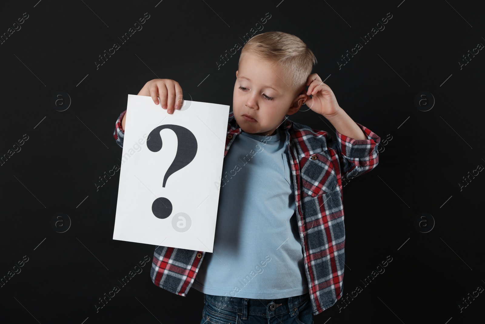 Photo of Confused boy holding sheet of paper with question mark on black background