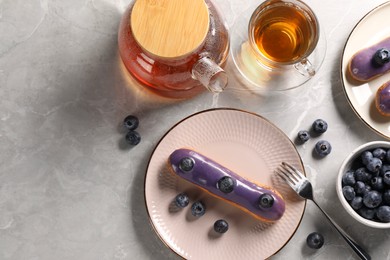 Photo of Tasty glazed eclair with blueberries and tea on grey marble table, flat lay. Space for text