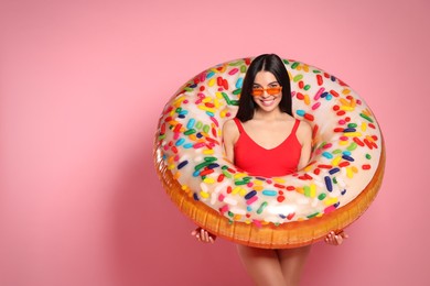 Photo of Young woman with stylish sunglasses holding inflatable ring against pink background. Space for text