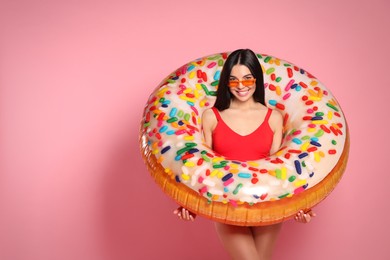 Young woman with stylish sunglasses holding inflatable ring against pink background. Space for text