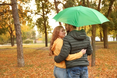 Photo of Happy couple with umbrella walking in park. Space for text
