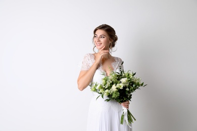 Young bride wearing wedding dress with beautiful bouquet on light background