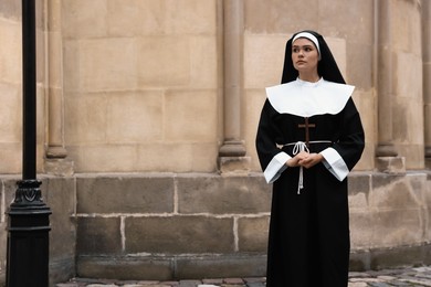 Photo of Young nun with Christian cross near building outdoors. Space for text
