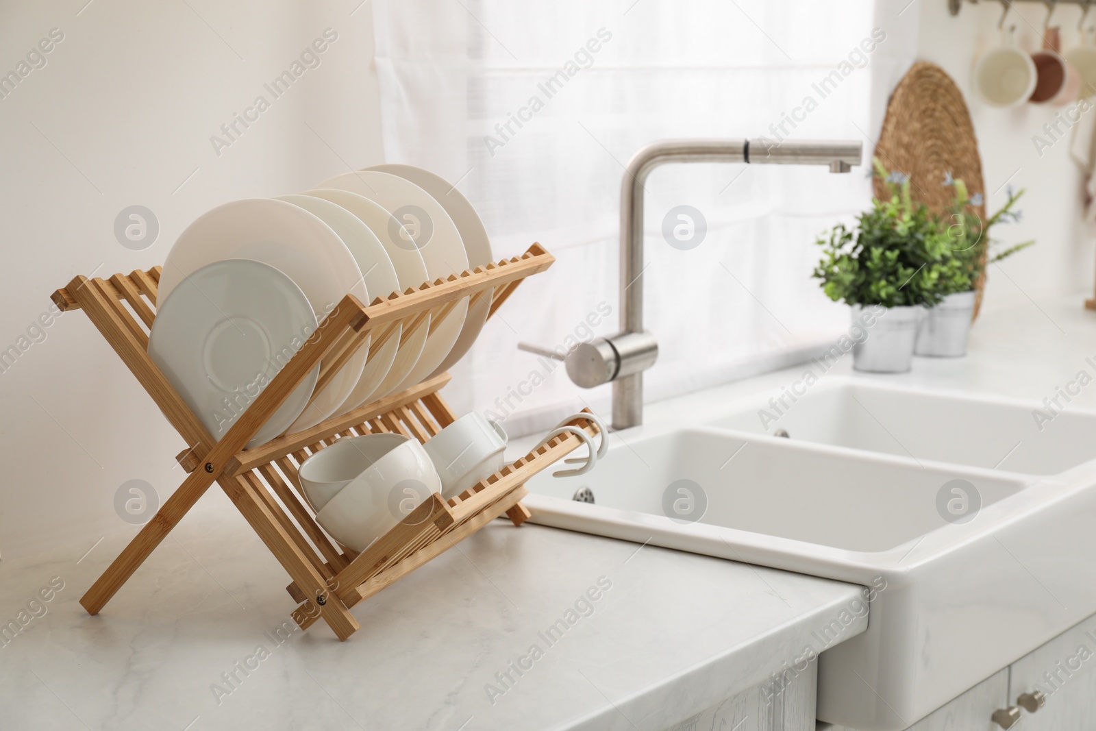 Photo of Drying rack with clean dishes on light marble countertop near sink in kitchen