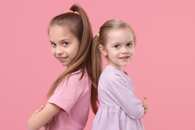 Portrait of cute little sisters on pink background