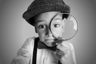 Little boy with magnifying glass playing detective on grey background, black and white effect