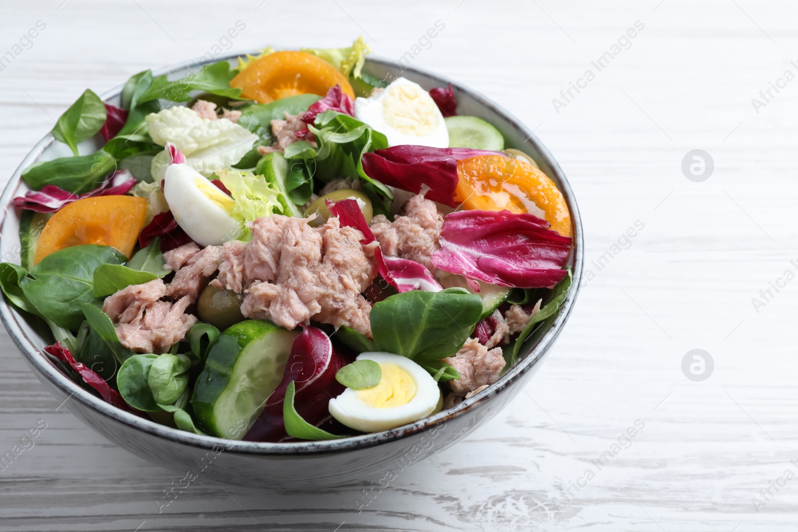 Photo of Bowl of delicious salad with canned tuna and vegetables on white wooden table