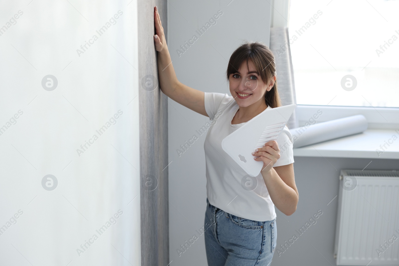 Photo of Woman with spatula hanging stylish gray wallpaper in room