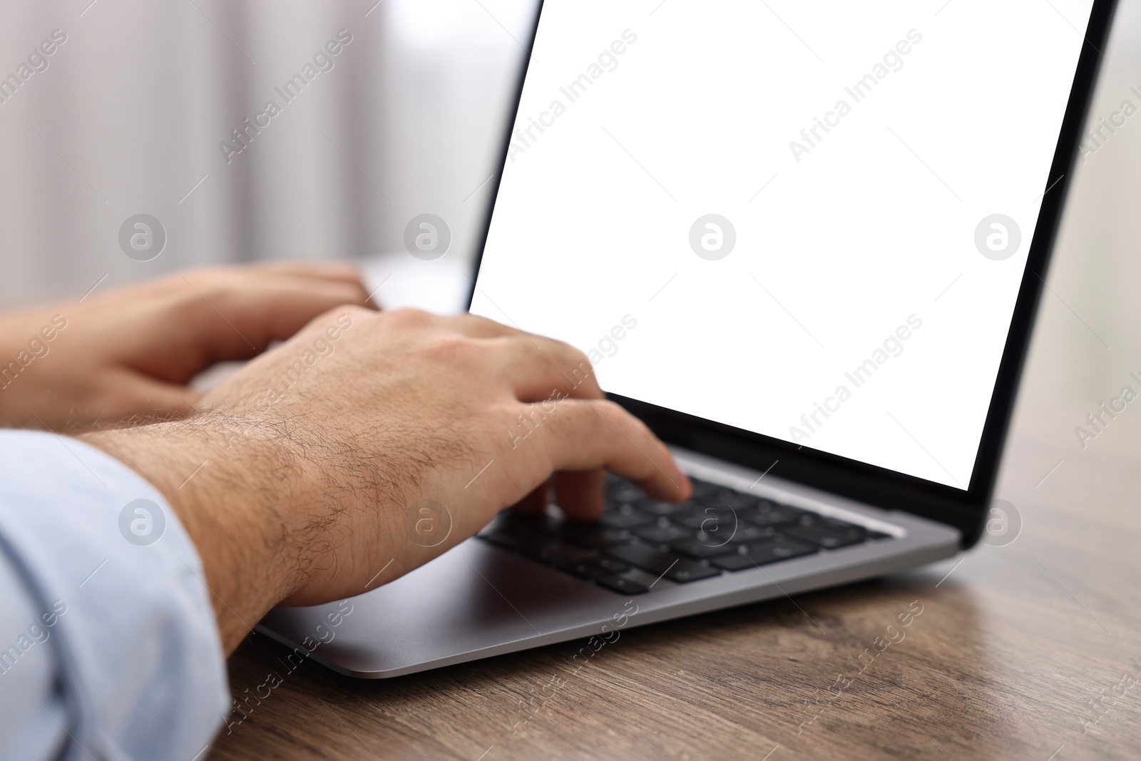 Photo of E-learning. Young man using laptop at wooden table, closeup