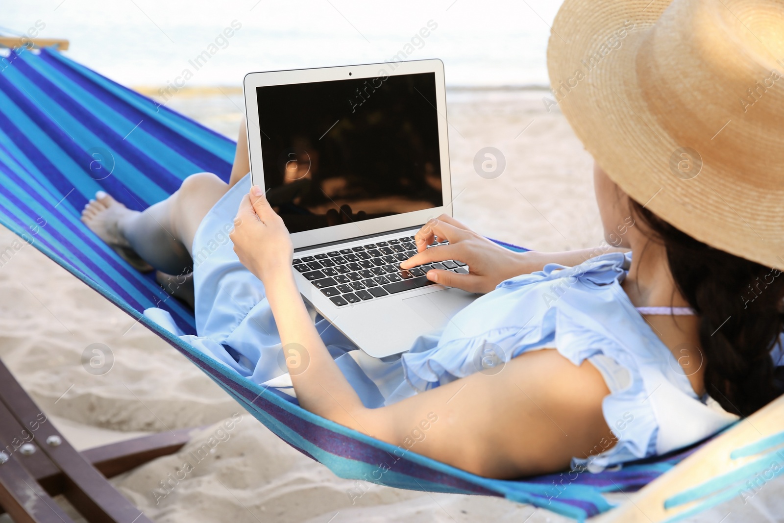 Photo of Young woman with laptop resting in hammock at seaside