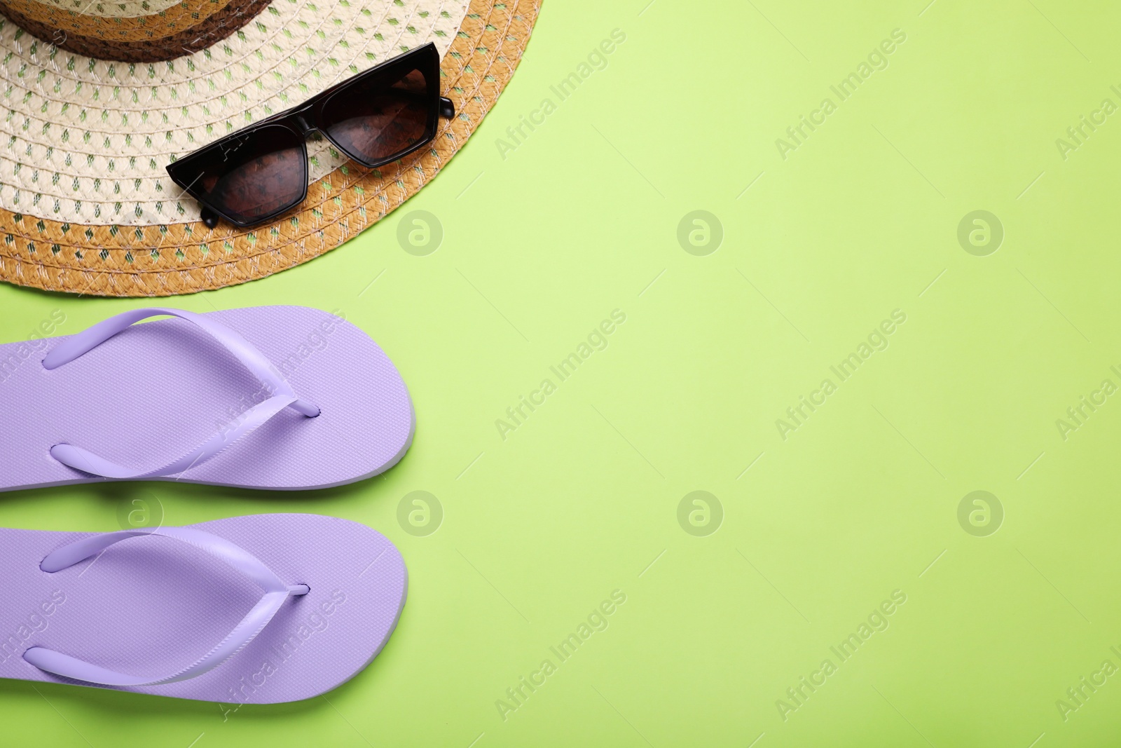 Photo of Stylish flip flops, sunglasses and hat on light green background, flat lay. Space for text