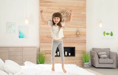 Photo of Cute little girl jumping on bed at home