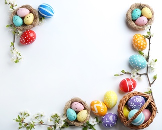 Photo of Composition with painted Easter eggs and blossoming branches on white background, top view