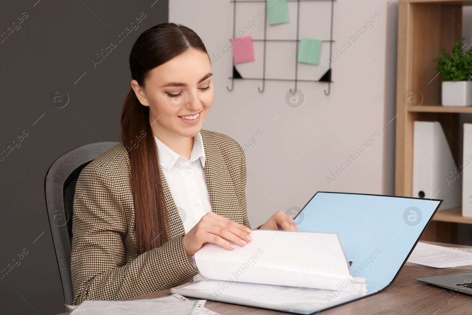Photo of Businesswoman putting document into file folder at wooden table in office