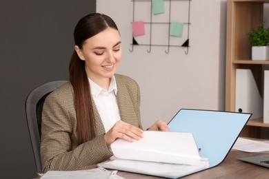 Photo of Businesswoman putting document into file folder at wooden table in office