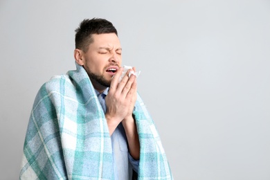 Man with plaid sneezing on light background, space for text. Runny nose