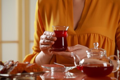 Photo of Woman holding glass of traditional Turkish tea at table indoors, closeup