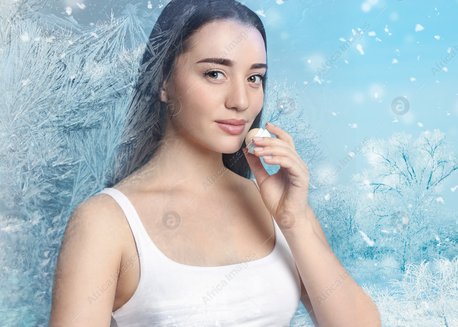 Image of Winter skin care. Woman applying lip balm, frost effect. Beautiful forest on background