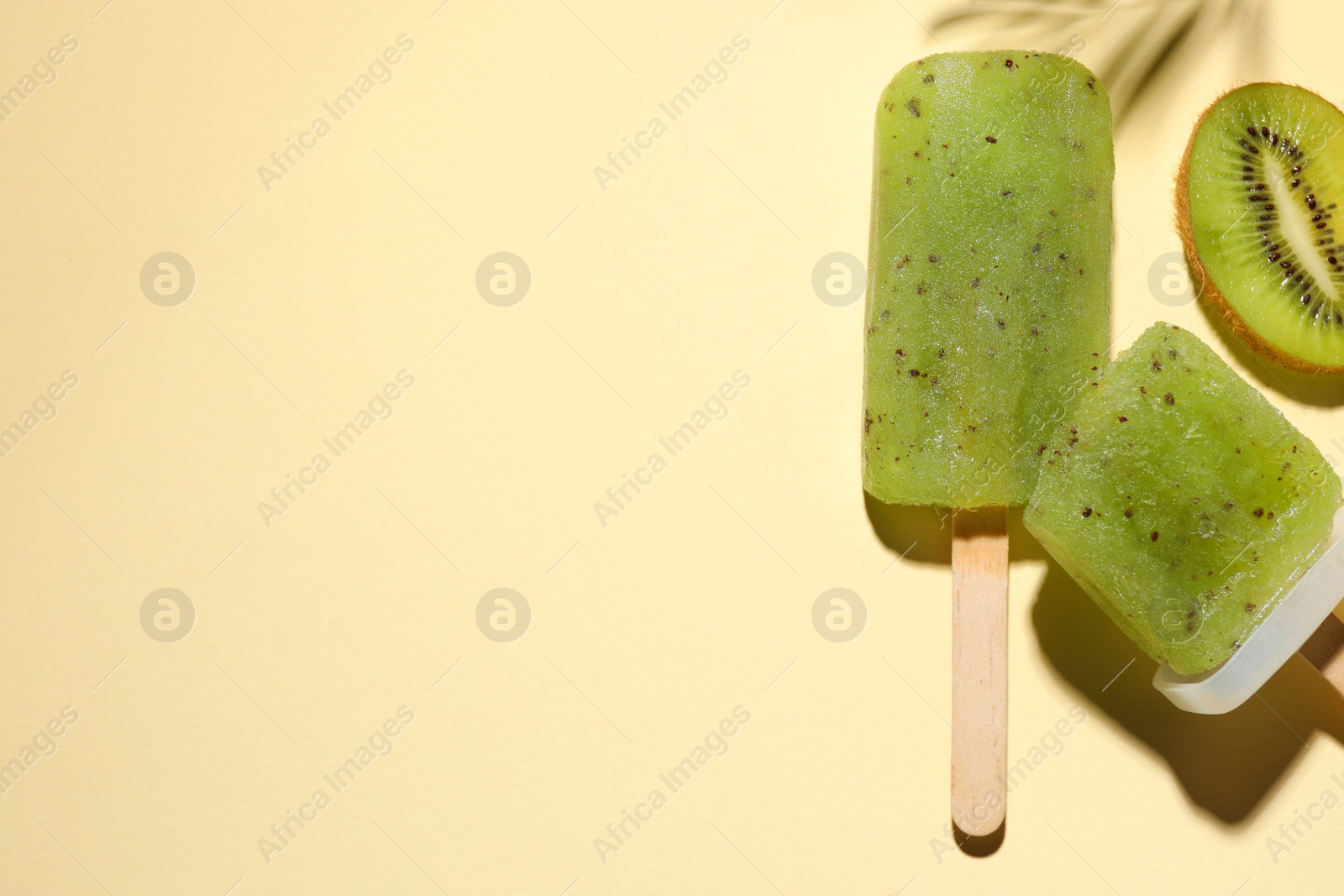 Photo of Tasty kiwi ice pops and space for text on pale light beige background, top view. Fruit popsicle