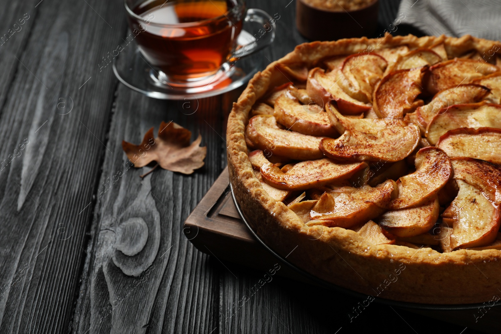 Photo of Delicious apple pie and cup of tea on black wooden table, closeup. Space for text