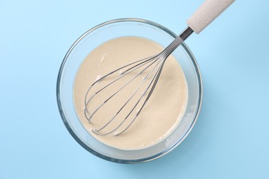 Photo of Dough and whisk in glass bowl on light blue background, top view