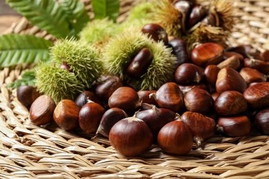 Photo of Fresh sweet edible chestnuts on wicker mat, closeup