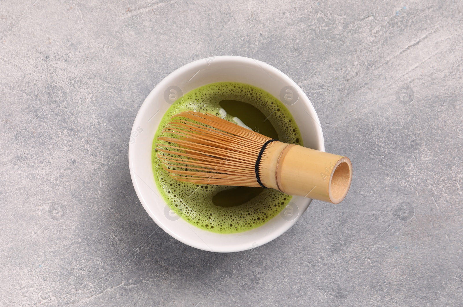 Photo of Cup of matcha tea and bamboo whisk on light gray textured table, top view