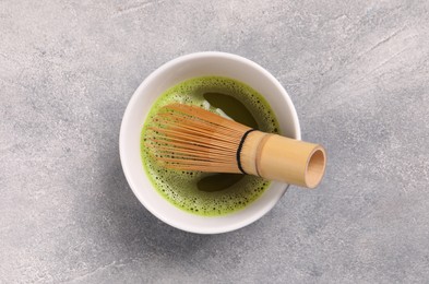 Cup of matcha tea and bamboo whisk on light gray textured table, top view