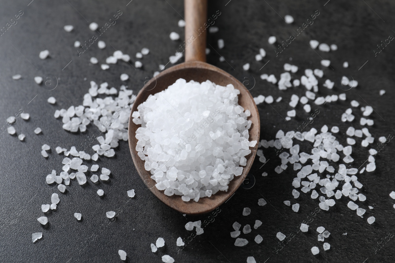 Photo of Natural salt and wooden spoon on black table, closeup