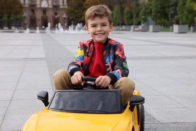 Cute little boy driving children's car on city street