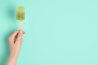 Photo of Woman holding delicious ice pop on turquoise background, closeup view with space for text. Fruit popsicle